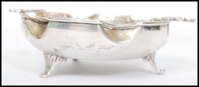 A vintage silver dish having a scalloped edge raised on tripod feet with central medallion depicting