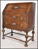 An early 20th century Jacobean revival oak bureau desk being raised on cup and cover legs united