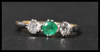 An 18ct gold and platinum three stone emerald and diamond ring having two 10pt diamonds with a