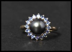 A 10ct gold and black pearl ring. The central black pearl having a halo of blue stones. Size S,