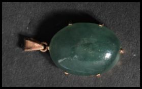 A vintage unmarked but tests as 9ct gold jade pendant. The large jade cabochon set to a pierced gold