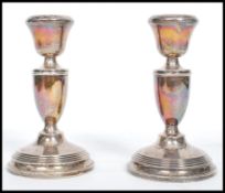 A silver hallmarked pair of candlesticks raised on terraced bases having trophy shaped stems and