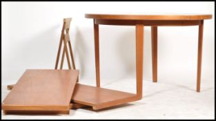 A 1970's retro teak wood circular dining table being raised on square legs. The extending table