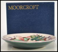 A Moorcroft ceramic pin tray coaster plate of circular form tube lined decorated with flowers in the