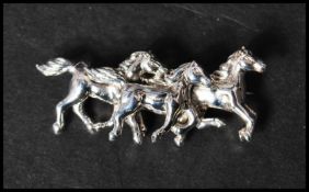 A 925 silver figural brooch in the form of galloping horses having a roller clip clasp. Measures 4.