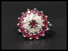A hallmarked 18ct white gold ruby and diamond cluster ring having a central raised ruby in claw