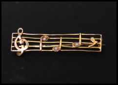 An early 20th century 9ct gold and seed pearl bar brooch in the form of  musical score notes. Marked