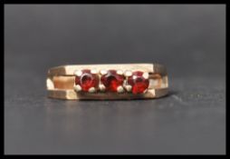 A hallmarked 9ct gold and red stone ring set with three red stones having split shoulders.