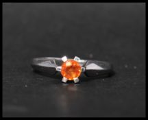 A hallmarked 9ct white gold solitaire ring set with a single round cut orange stone. Hallmarked
