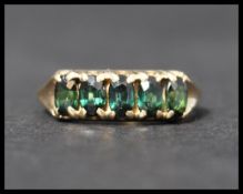 A hallmarked 9ct gold 5 stone ring set with 5 oval cut dark green stones in a gypsy setting.