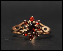 A hallmarked 9ct gold and garnet cluster ring with diamond cut pierced shoulders. Hallmarked