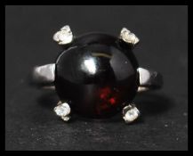 A hallmarked 9ct white gold, garnet and white stone ring set with a garnet cabochon with four accent