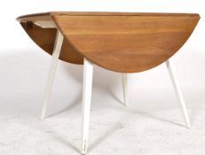 A retro mid century beech and oak Ercol drop leaf dining table being raised on squared legs with