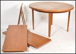 A 1970's retro teak wood circular dining table being raised on square legs. The extending table