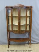 An Edwardian inlaid mahogany bow fronted glazed cabinet with undershelf raised on tapering legs and