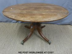 A late 19th/ early 20th century oval dining room table on turned pedestal base with four brass lion