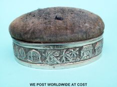 A George V hallmarked silver pin cushion with an embossed landscape scene,