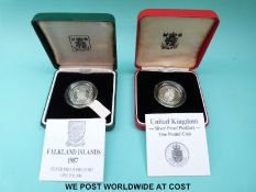 Two cased silver proof Piedfort £1 coins comprising a 1987 Falklands example and 1988 UK emblem,