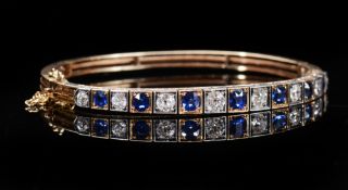 A yellow metal bangle set with alternating diamonds and sapphires,