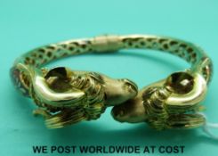 A yellow metal bracelet marked 15k in the form of two ram's heads set with emerald eyes and red