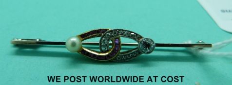 A white metal brooch set with rubies, diamonds and a pearl in an entwined design,