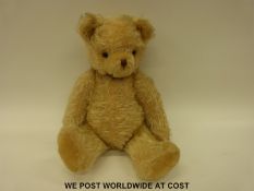 A vintage teddy bear with blonde mohair body, shaved snout, hump back, cocked feet and glass eyes,