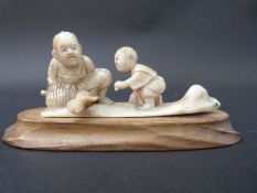 A Japanese Meiji period carved ivory okimono of a child with father, on wooden plinth,