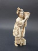 A Japanese Meiji period carved ivory okimono of a lady carrying a basket of clams, 13.