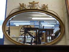 A gilt framed oval mirror decorated with mythical creatures either side of an urn with swags,