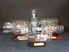 A collection of glass art ships in bottles on wooden stands, including HMS Discovery, tea clipper,