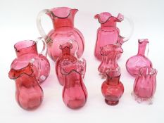 Ten cranberry glass jugs, some with etched decoration, all with applied clear handles,