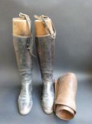 A pair of vintage leather riding boots with wooden trees and brass suspension loops,