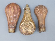 Three copper and brass powder flasks, all with embossed decoration, largest 17.5cm long.