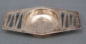 A modern hallmarked silver tea strainer with pierced retro design to handles,