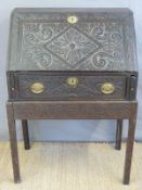 An antique oak bureau on stand with carved decoration and drawer below,