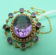 An Edwardian 9ct gold brooch set with a central amethyst surrounded by a band of seed pearls and a