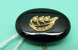 An onyx brooch set with seed pearls and a glass photo compartment to the back