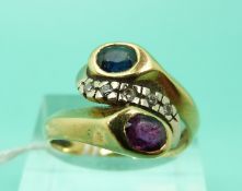 A yellow metal ring set with a sapphire and a ruby with diamonds between them in a twist setting
