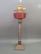 A silver plated Corinthian column oil lamp with red glass reservoir,