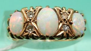 A 9ct gold ring set with three oval opal cabochons and four diamonds (Size L)