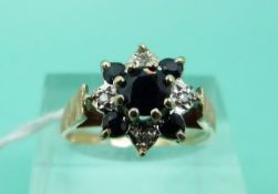 A 9ct gold ring set with a central sapphire surrounded by alternating diamonds and sapphires (Size