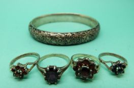A silver bangle with foliate decoration and four silver rings set with garnets.