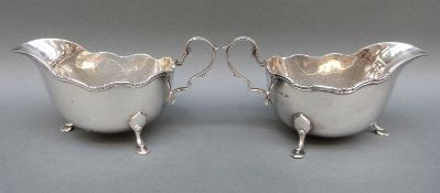 A pair of Harrods Elizabeth II hallmarked silver sauce boats with shaped edge raised on three hoof