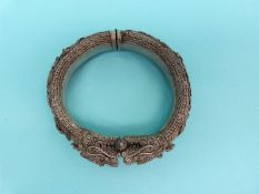 A Chinese white metal filigree bangle in the form of two dragons with raised floral decoration