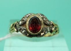 A Victorian yellow metal ring set with an oval garnet surrounded by diamonds (Size P)