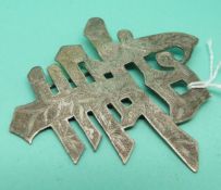 A white metal brooch in the form of Chinese characters with engraved detail.