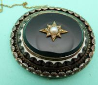 A Victorian mourning brooch set with black onyx, seed pearl and diamonds within an enamel border,