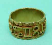 A yellow metal ring with symbols/ letters around the band and a foliate border