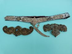 A white metal belt buckle with sections of sphere decoration with a filigree knife hanging,