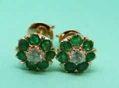 A pair of gold earrings set with a diamonds surrounded by emeralds to each